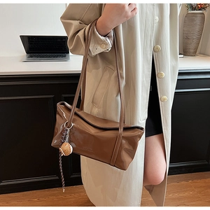 Detail of a brown patent leather shoulder bag with a mirror finish and brand logo