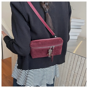 Detail view of burgundy suede crossbody bag featuring unique robot charm and zipper