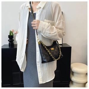 Detail of black quilted leather shoulder bag with gold chain strap on a model