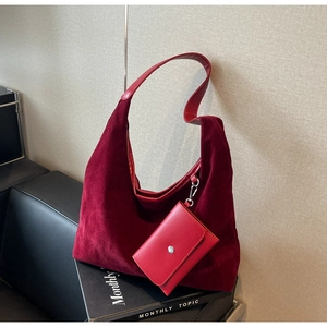 Detail of burgundy velvet tote bag with a matching leather pouch against a wall
