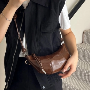 Minimalist dark brown patent leather croissant bag with knotted strap on model shoulder