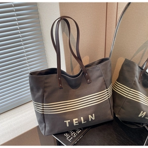 Close-up of a large grey canvas tote bag with brown leather handles and TELN logo print