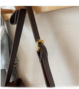 Detail of adjustable deep brown faux leather shoulder strap with golden metal buckle
