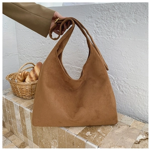 Detail of a large brown suede tote bag with a wide shoulder strap in a warm setting