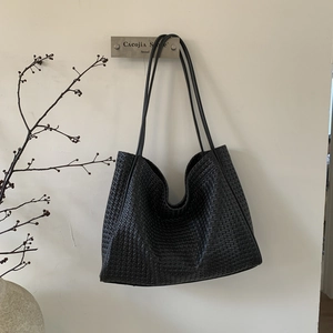 Détail d'un sac cabas en cuir tressé noir suspendu au mur avec une esthétique minimaliste