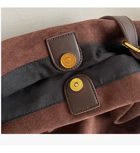 Detailed close-up of brown suede fabric with gold magnetic buckles and leather stitching