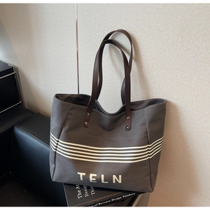 Detail of grey canvas tote bag with white stripes, brown leather handle and silver rivets