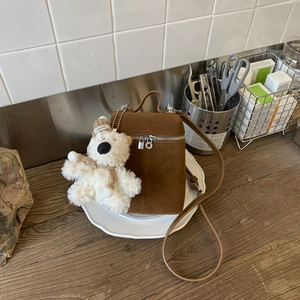 Detail einer braunen Wildleder-Beuteltasche mit süßem Teddybär-Anhänger auf weißem Tablett