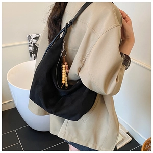 Detail einer schwarzen Umhängetasche aus Segeltuch mit Perlenanhänger am beigen Blazer