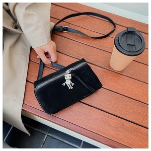 Detail of black suede crossbody bag with silver robot charm on a wooden bench
