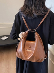 Brown faux leather tote bag with plush charm shown on person wearing black coat