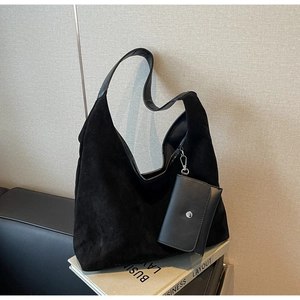 Detail of black suede hobo bag and matching small wallet on books in minimalist setting