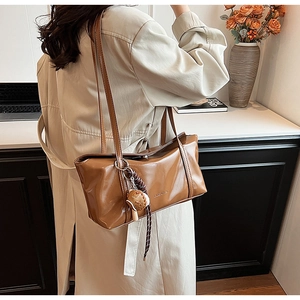 Detail view of caramel brown leather shoulder bag with a cute bread shaped charm accessory