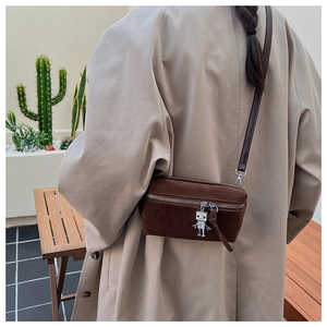 Detail of dark brown suede mini crossbody bag featuring a unique silver robot charm accessory