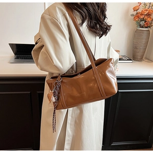 Close-up of caramel glossy leather shoulder bag with chic woven heart charm on the desk