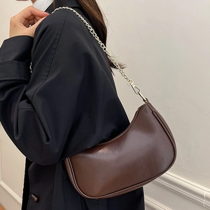 Deep brown crescent moon underarm bag with gold chain strap on model in soft indoor light