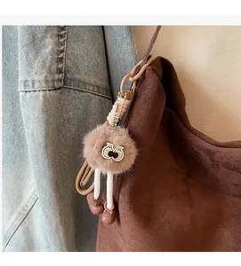 Brown furry monster bag charm with big eyes and rope legs on a stylish tote bag