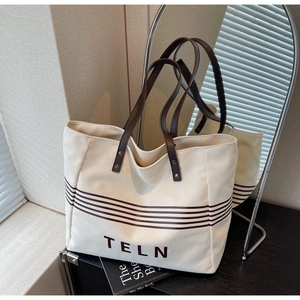 Detailed close-up of beige canvas tote with brown stripes, leather straps and metal rivets