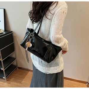 Detailed close-up of a black glossy patent leather shoulder bag with a baseball charm