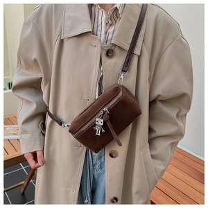 Detail of vintage brown suede crossbody bag with a metal robot pendant on beige trench coat