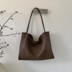 Détail du tissage marron foncé sur un grand sac cabas en similicuir suspendu au mur