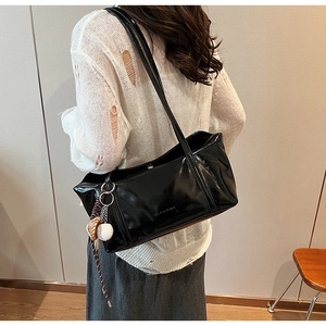 Close-up of glossy black patent leather tote bag with CLEAKOK logo and baseball charm