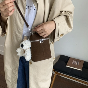 Detail der braunen Wildleder-Zylindertasche mit Silberreißverschlüssen und Bärenanhänger