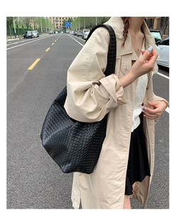Fashionable black woven leather hobo bag styled with a beige trench coat for a casual look