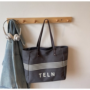 Detail of grey canvas tote bag with white stripes and dark brown leather straps on hanger