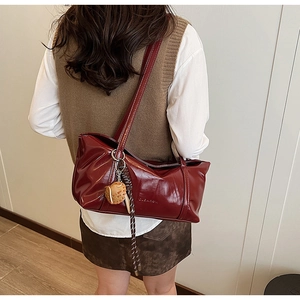 Deep red leather tote bag with brand embossing and owl charm shown on a model