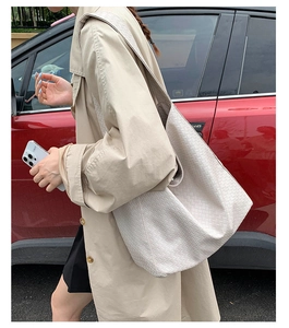 Detail of large woven hobo shoulder bag in cream color worn with khaki trench coat