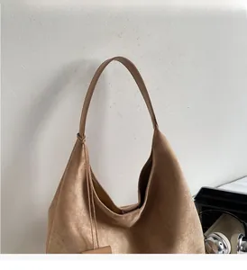 Detail of camel suede hobo bag with side leather tag in a cozy lifestyle setting