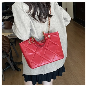 Sac fourre-tout matelassé rouge avec chaîne dorée porté par un mannequin dans un café