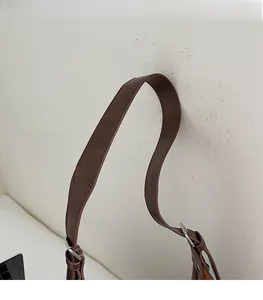 Detail of adjustable dark brown faux suede shoulder strap with silver buckle and stitching