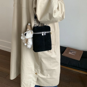 Detail einer schwarzen Wildleder-Umhängetasche mit einem plüschigen weißen Bären-Anhänger