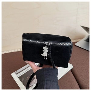 Detail of black suede bag featuring a silver metal robot zipper charm and textured finish