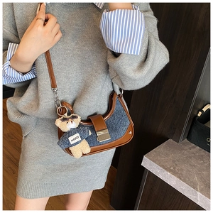 Detail of denim and leather crescent bag featuring a stylish teddy bear charm accessory