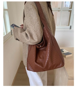 Brown woven leather tote bag shown on model's shoulder in a minimalist indoor setting