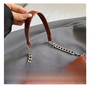 Close-up of brown glossy leather bag showing soft handle and silver chain detail