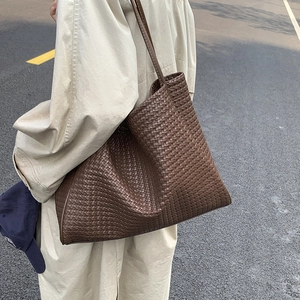 Détail de la texture en cuir marron tressé et des longues bandoulières sur un sac cabas