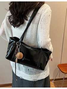 Minimalist black patent leather hobo bag with yellow charm and embossed text on side