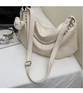 Detail einer cremeweißen Halbmond-Tasche mit Silberkette und Plüschbär-Anhänger