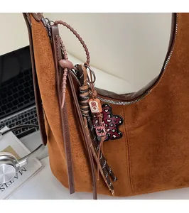 Close-up of brown suede crossbody bag with decorative braided knot and cute bear pendant
