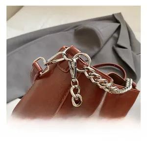 Close-up of brown oiled leather bag with thick silver metal chain and hook hardware