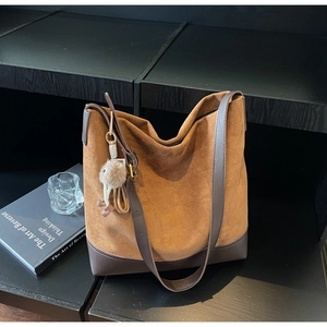 Close-up of brown suede tote bag featuring leather straps and a decorative plush charm