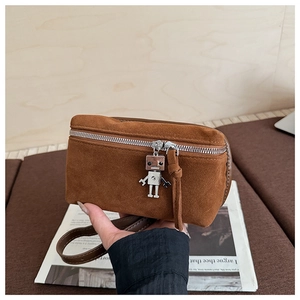 Detail of a brown suede crossbody bag featuring a unique silver metal robot charm