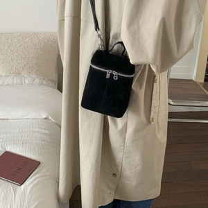 Detailansicht einer mattschwarzen Beuteltasche getragen zu einem beigen Trenchcoat