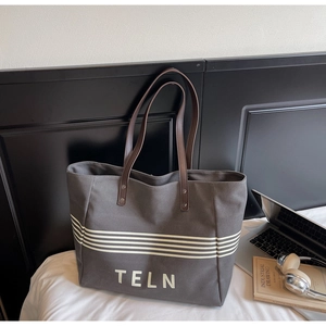 Detail of grey canvas tote bag with white stripes and brown leather handles on a bed