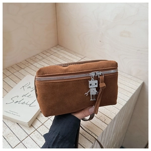 Detail of a brown suede crossbody bag with a robot charm and silver hardware on a ledge