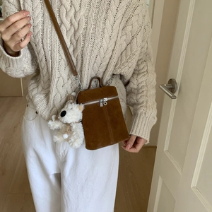 Braune Wildleder-Eimertasche mit Plüschbär-Anhänger an Modell mit beigem Strickpullover